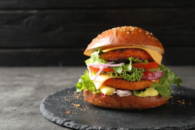 Photo of Slate plate with double vegetarian burger on table against dark background