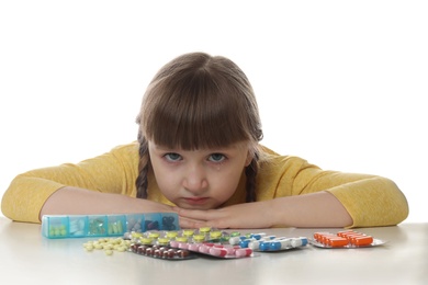 Photo of Crying little child with many different pills on white background. Danger of medicament intoxication