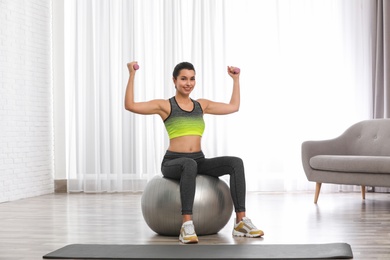 Photo of Young woman doing exercise with dumbbells on fitness ball at home