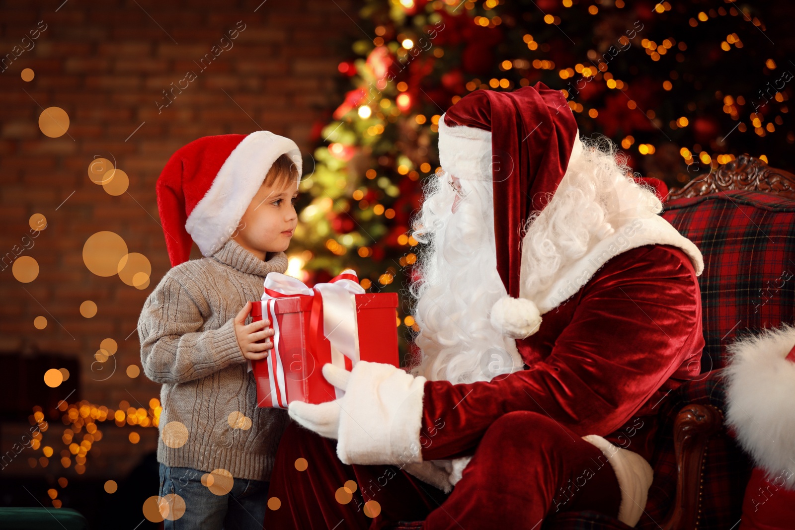 Photo of Santa Claus and little boy with gift near Christmas tree indoors