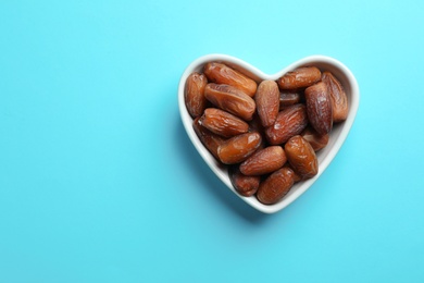 Photo of Heart shaped bowl with sweet dried date fruits on color background, top view. Space for text