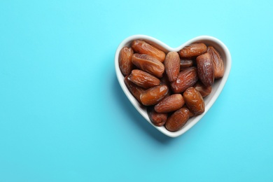 Heart shaped bowl with sweet dried date fruits on color background, top view. Space for text