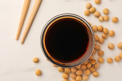 Soy sauce in bowl, soybeans and chopsticks on white table, flat lay