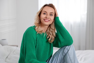 Happy woman in stylish warm sweater on bed at home