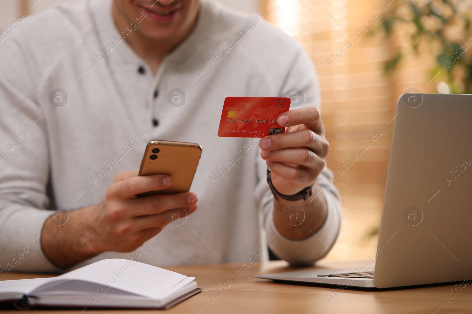 Photo of Man using smartphone and credit card for online payment at desk indoors, closeup