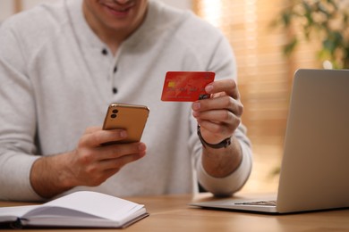 Man using smartphone and credit card for online payment at desk indoors, closeup