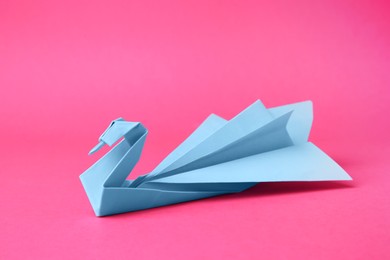 Photo of Light blue paper swan on pink background. Origami art