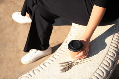 Photo of Woman with cardboard cup of coffee sitting on stone bench outdoors, closeup