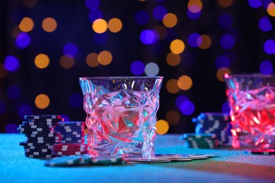 Photo of Alcohol drink, playing cards and casino chips on table against blurred lights