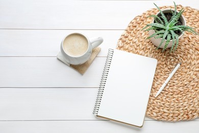 Mug of coffee with stylish cup coaster, houseplant and notebook on white wooden table, flat lay. Space for text