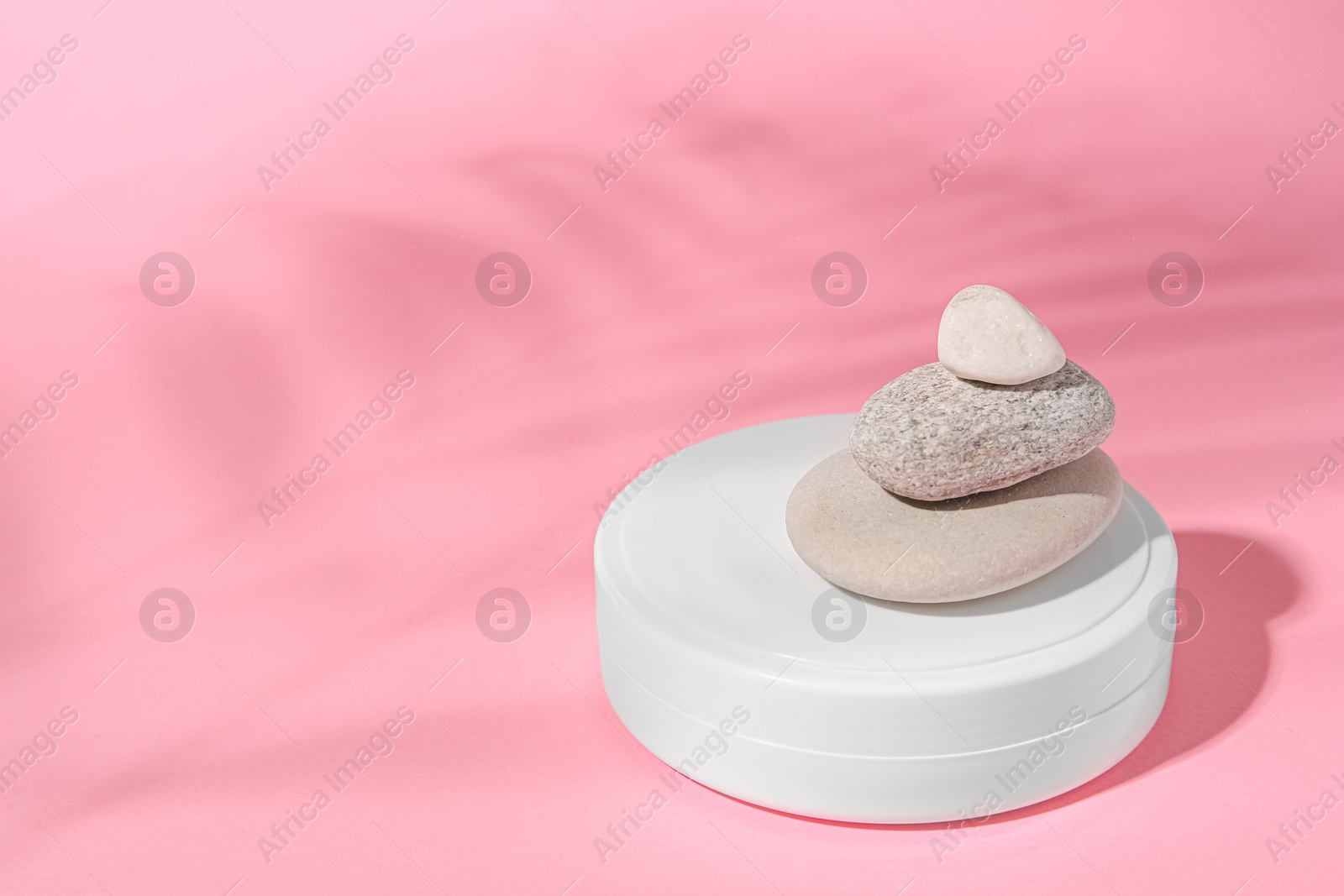 Photo of Cosmetic product, stacked stones and shadow of tropical leaf on pink background. Space for text