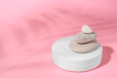 Photo of Cosmetic product, stacked stones and shadowtropical leaf on pink background. Space for text