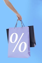 Image of Woman holding paper shopping bag with percent sign on light blue background, closeup. Discount concept