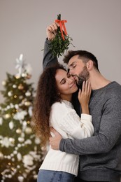 Photo of Happy man kissing his girlfriend under mistletoe bunch in room decorated for Christmas