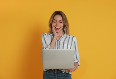 Young woman with modern laptop on yellow background