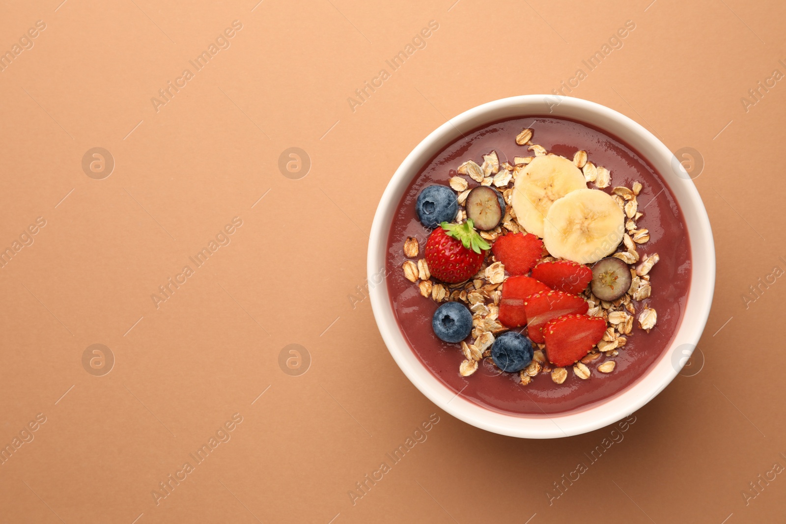 Photo of Delicious smoothie bowl with fresh berries, banana and granola on pale orange background, top view. Space for text