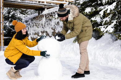 Happy couple making snowman together outdoors. Winter vacation