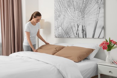 Photo of Young woman making bed in room. Space for text