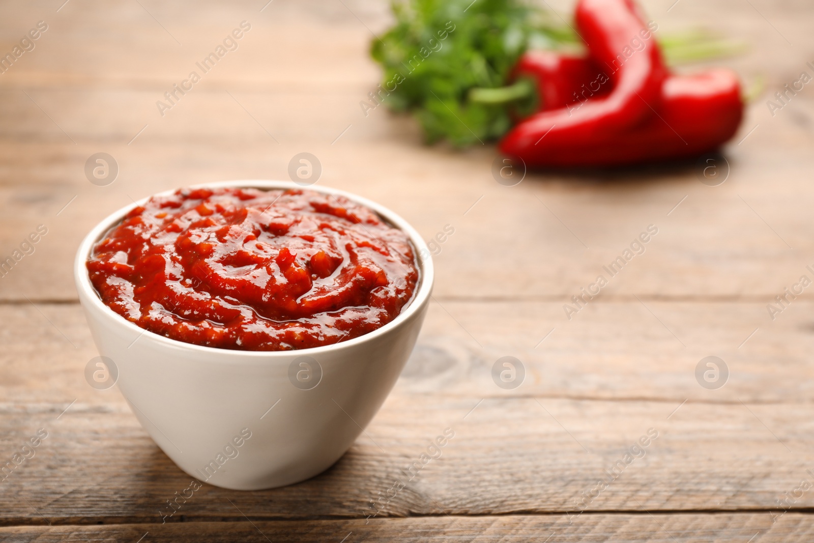 Photo of Delicious adjika sauce in bowl on wooden table, closeup. Space for text