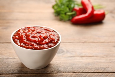 Delicious adjika sauce in bowl on wooden table, closeup. Space for text