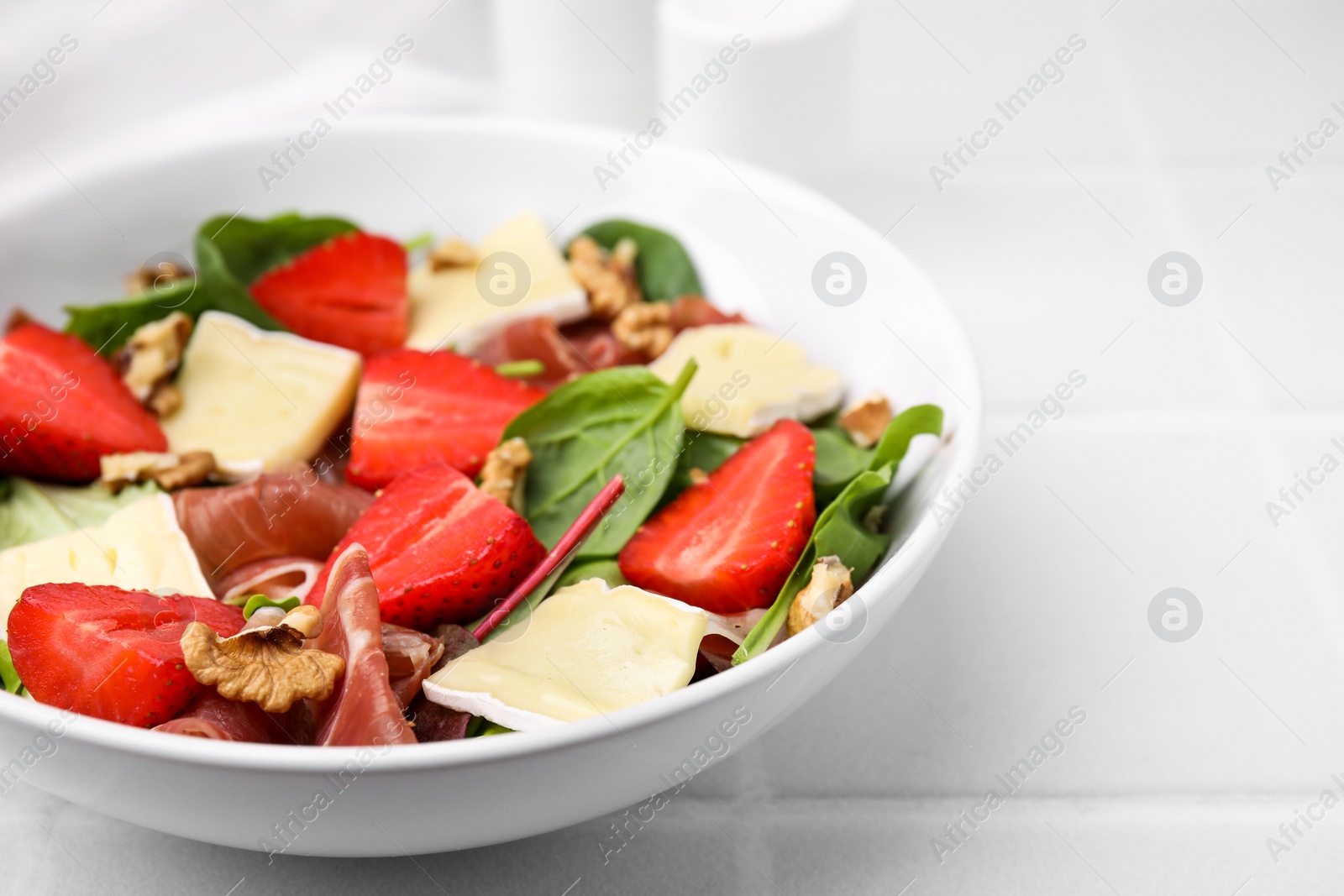 Photo of Tasty salad with brie cheese, prosciutto, strawberries and walnuts on white table, closeup. Space for text