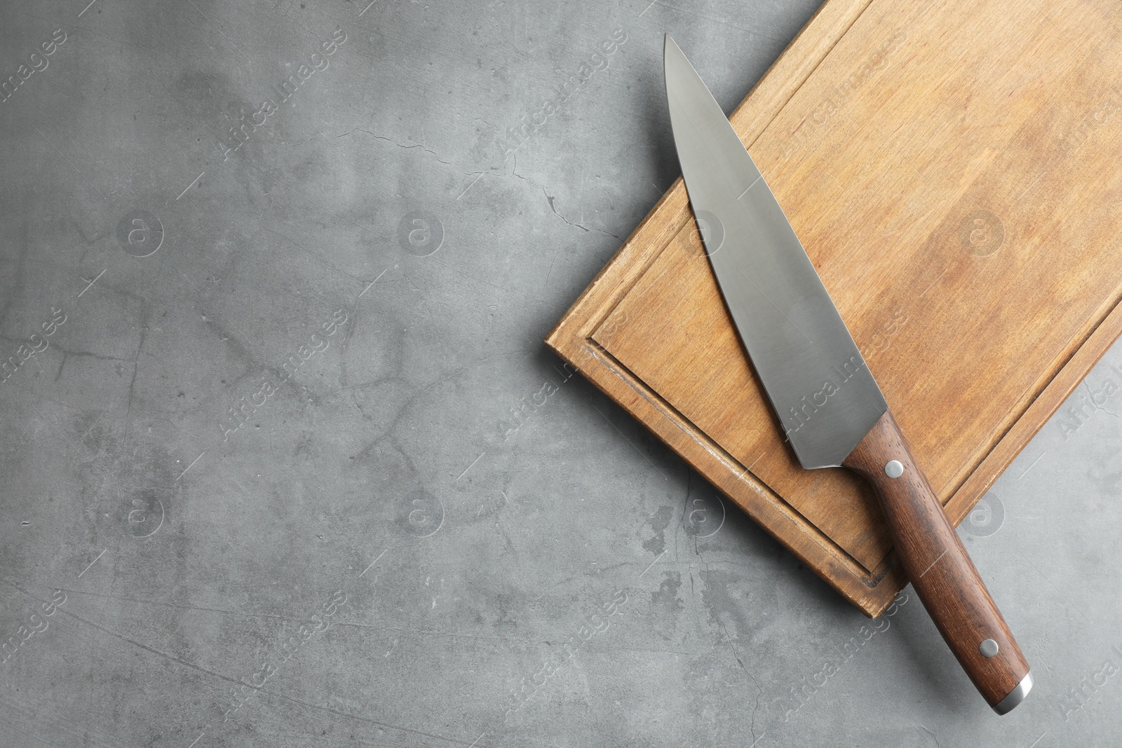 Photo of Knife and wooden board on grey textured table, top view. Space for text