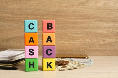 Photo of Colorful cubes with word Cashback and money on wooden table, space for text