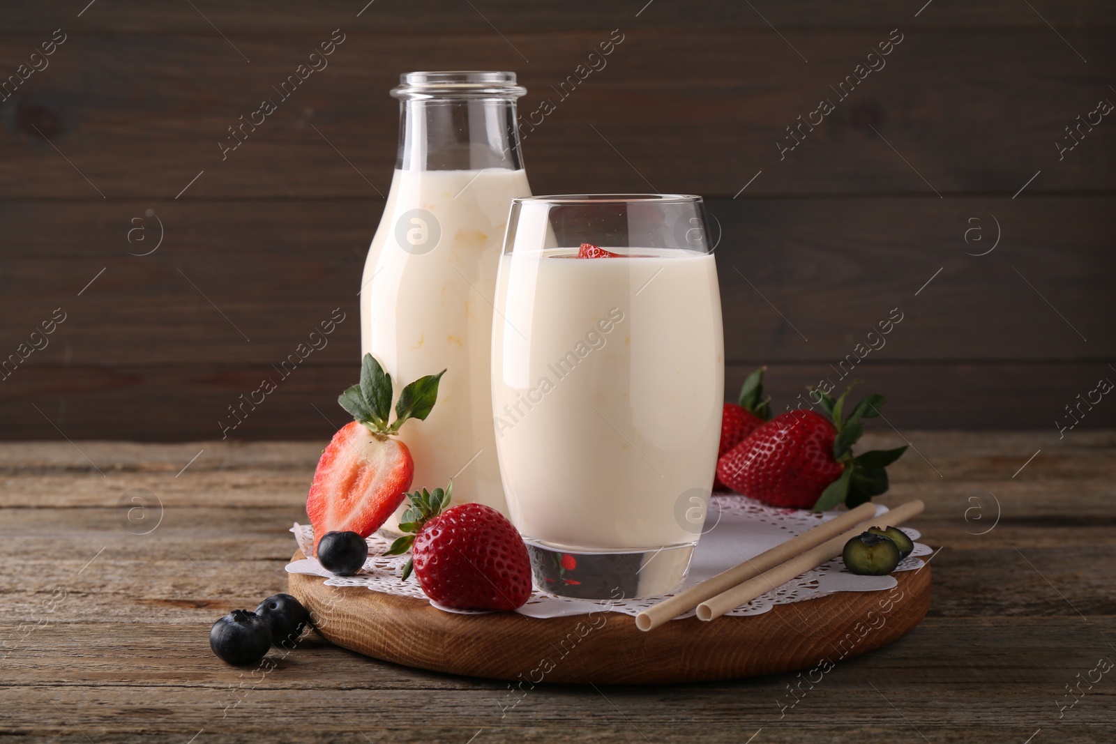 Photo of Tasty yogurt in glass, bottle, straws and berries on wooden table