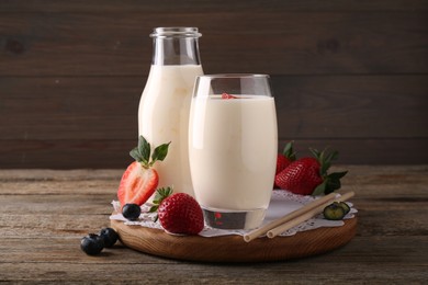 Tasty yogurt in glass, bottle, straws and berries on wooden table