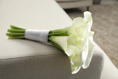 Beautiful calla lily flowers tied with ribbon on sofa indoors