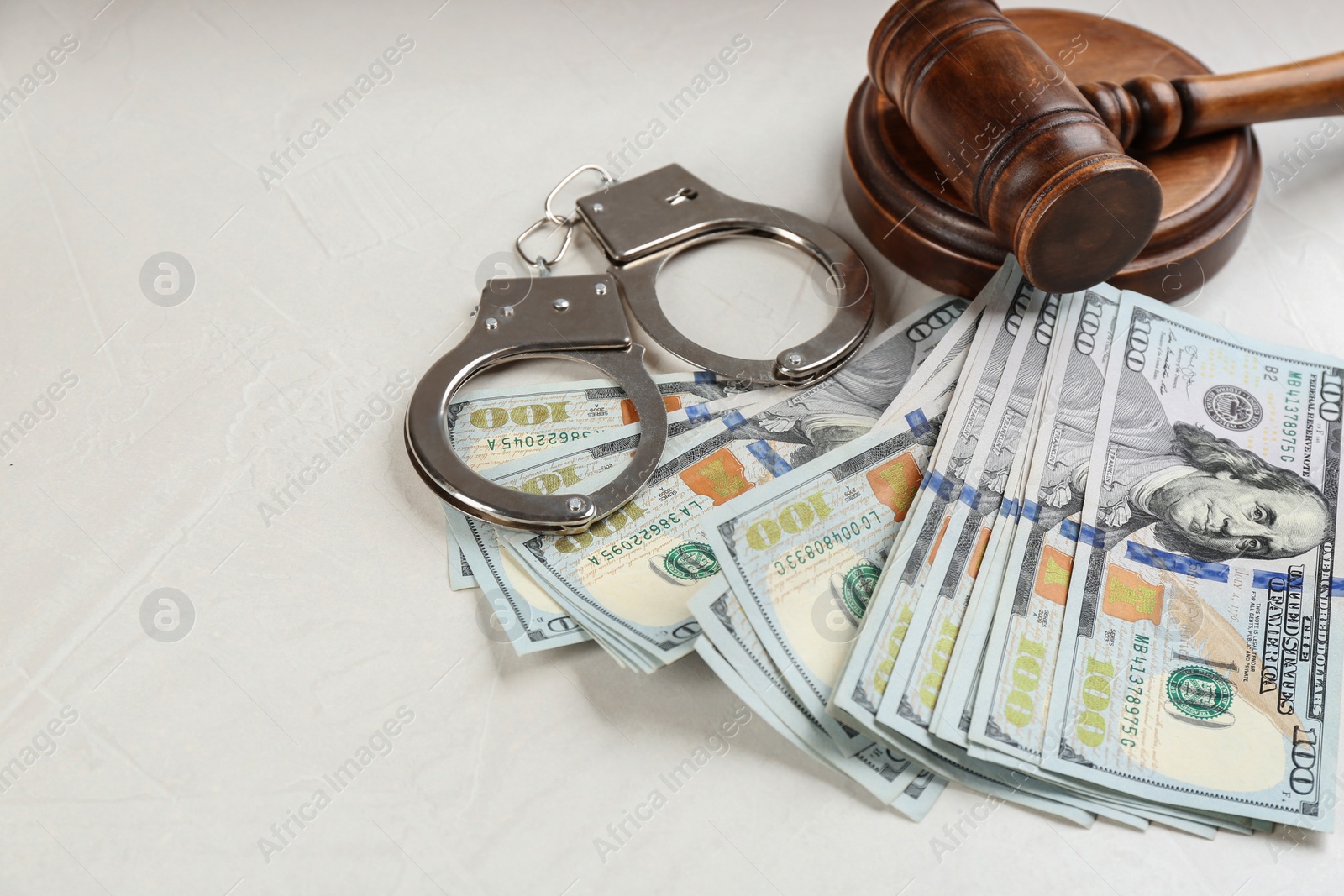 Photo of Dollar bills, gavel and handcuffs on light grey stone table. Bribe concept