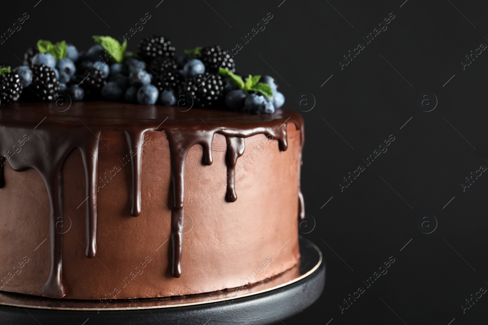 Photo of Fresh delicious homemade chocolate cake with berries on dessert stand against dark background