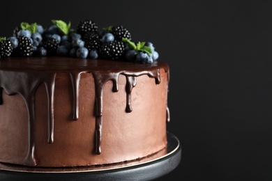 Photo of Fresh delicious homemade chocolate cake with berries on dessert stand against dark background