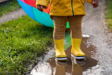 Photo of Little girl wearing rubber boots standing in puddle, closeup