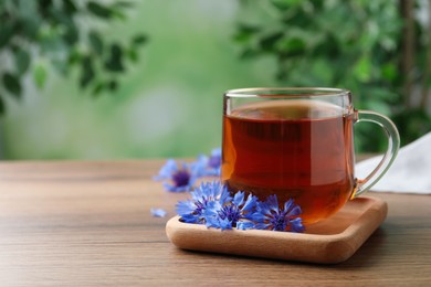 Photo of Glass cup of tea and cornflowers on wooden table. Space for text