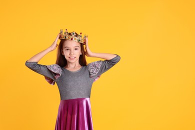 Photo of Cute girl in dress and golden crown with gems on yellow background, space for text. Little princess