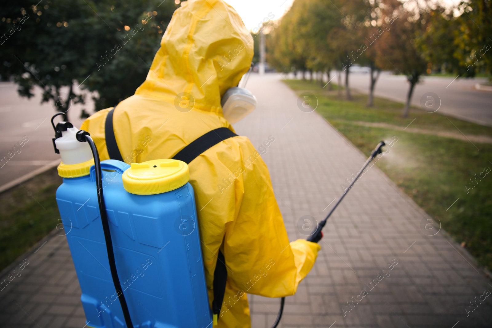 Photo of Person in hazmat suit disinfecting street with sprayer, back view. Surface treatment during coronavirus pandemic