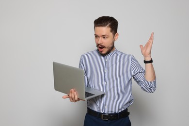 Emotional man looking at laptop on light grey background