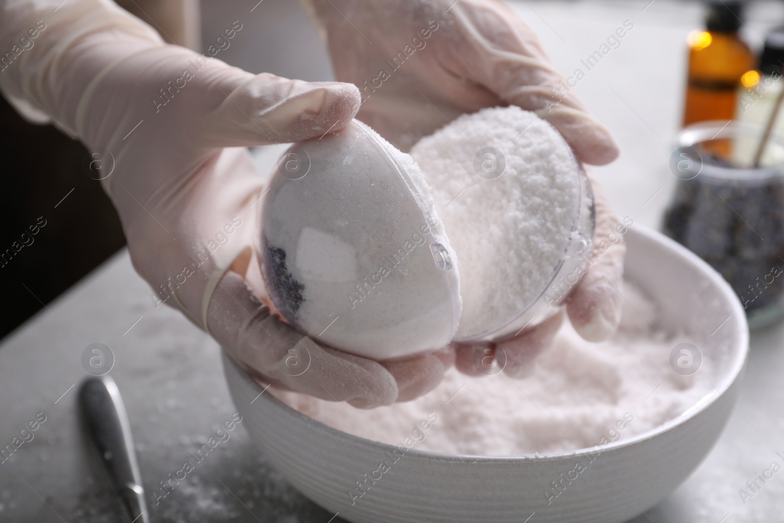 Photo of Woman in gloves making bath bomb at grey table, closeup