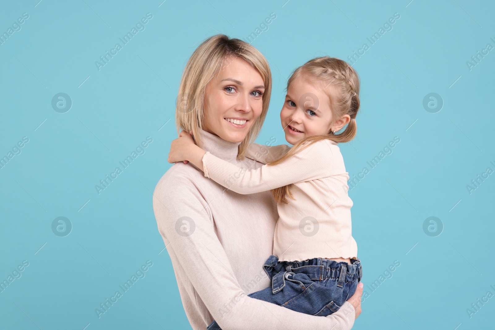 Photo of Daughter hugging her happy mother on light blue background