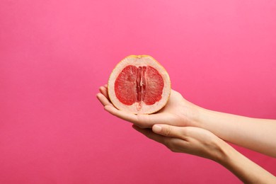 Photo of Woman holding half of grapefruit on pink background, closeup. Sex concept
