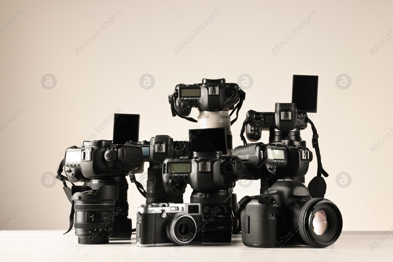 Photo of Modern cameras on white wooden table against light background