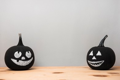 Photo of Halloween celebration. Black pumpkins with drawn spooky faces on wooden table, space for text
