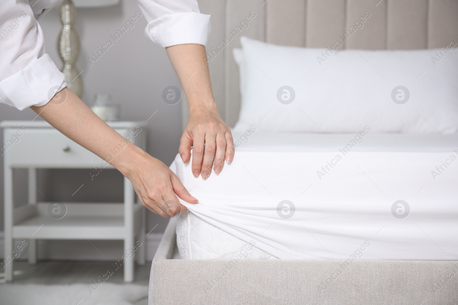 Photo of Woman putting white fitted sheet over mattress on bed indoors, closeup