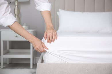 Woman putting white fitted sheet over mattress on bed indoors, closeup