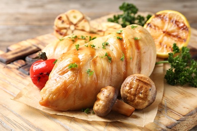 Photo of Wooden board with grilled chicken breasts and garnish on table, closeup