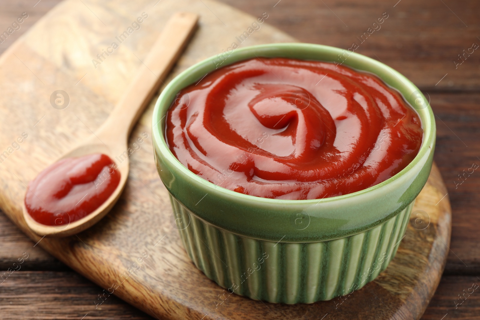 Photo of Bowl and spoon of tasty ketchup on wooden table, closeup
