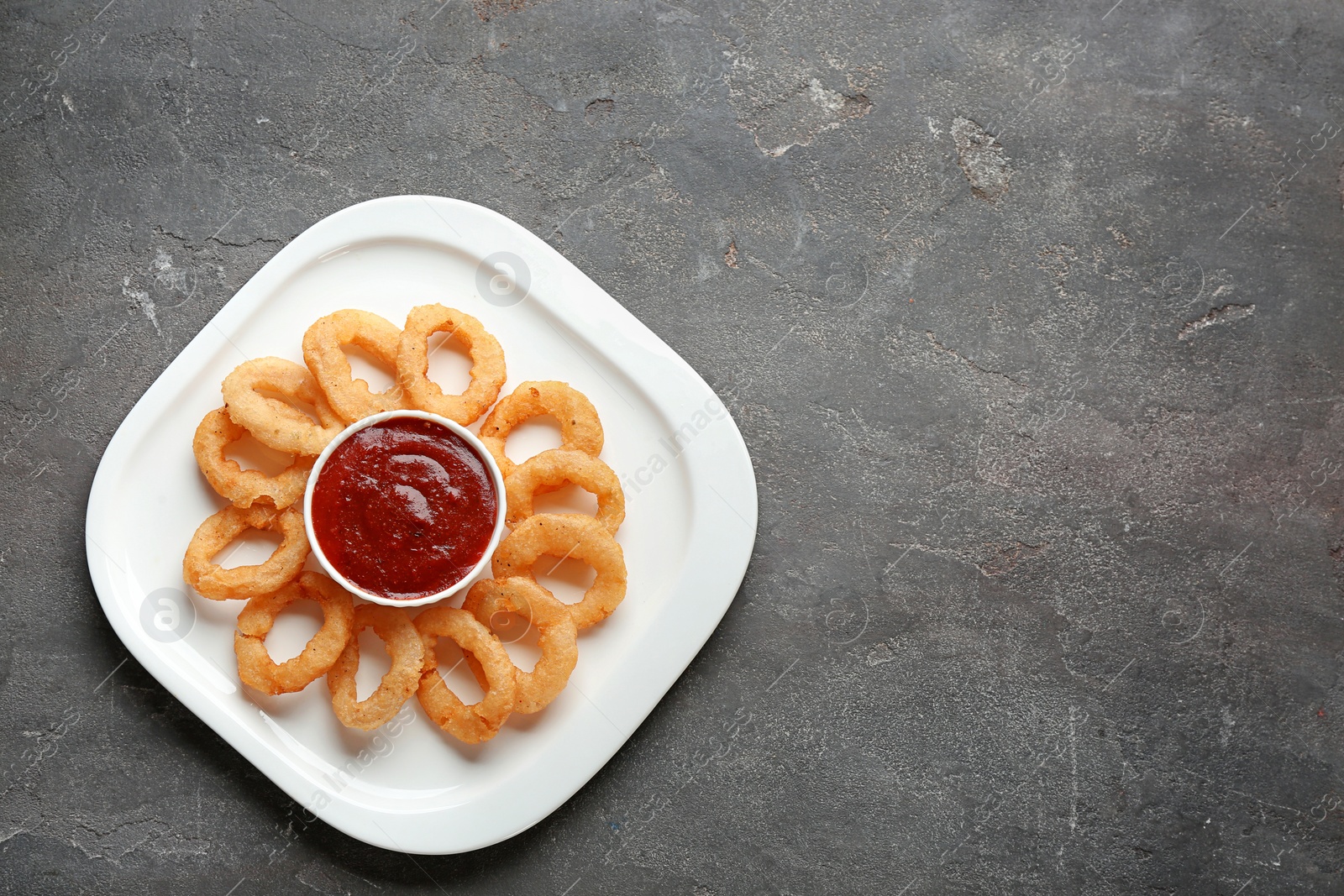 Photo of Plate with fried onion rings and sauce on table, top view