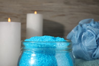 Aromatic sea salt, burning candles and shower puff on wooden background, closeup