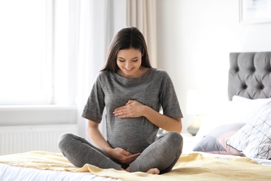 Photo of Young pregnant woman sitting on bed at home